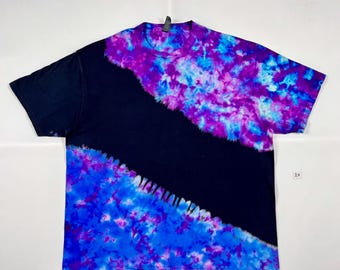 Puede incluir: Una camiseta negra con un diseño dividido en diagonal. Un lado es negro, el otro lado está teñido en tonos de azul, morado y blanco. La camiseta está etiquetada con "2X".