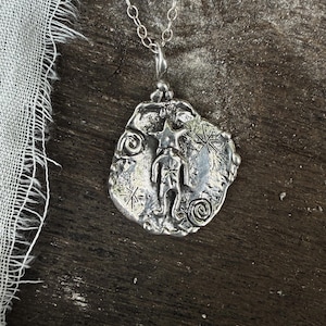May include: A silver necklace with a pendant featuring a stylised human figure with a star above its head. The pendant is textured and has a rustic look.