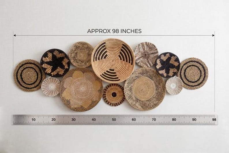 May include: A collection of twelve round woven wall baskets in natural tan, brown, and black tones with various geometric patterns. A metal ruler at the bottom indicates a total width of approximately 249 cm for the entire arrangement.
