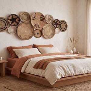 May include: A collection of round, woven wall baskets in various sizes and natural earth tones, including tan, beige, and dark brown, arranged in a cluster above a low-profile wooden bed frame with layered bedding in shades of cream and rust.