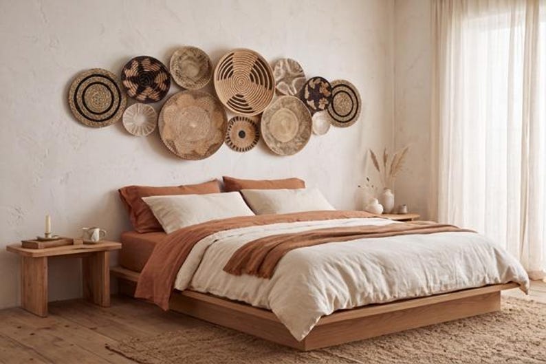 May include: A collection of round, woven wall baskets in various sizes and natural earth tones, including tan, beige, and dark brown, arranged in a cluster above a low-profile wooden bed frame with layered bedding in shades of cream and rust.
