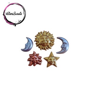 May include: A set of five gold and silver celestial-themed cake toppers. The set includes a sun, a moon, and three stars. The sun and moon have faces, and the stars are five-pointed.