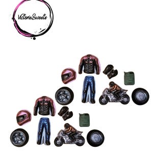 May include: A collection of miniature motorcycle-themed decorations, including helmets, jackets, trousers, tyres, gloves, fuel cans, and motorcycles. The decorations are in shades of pink, black, silver, and blue. The image includes the text "Victorie Sweets" in a circular logo.