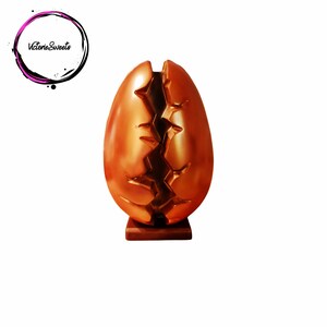 May include: A large, cracked, golden chocolate egg on a wooden base. The egg is split open, revealing the inside.