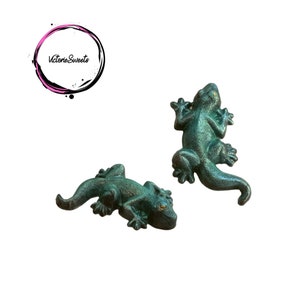 May include: Two green metal gecko figurines. The geckos are in a realistic pose with detailed features.