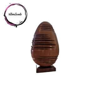 May include: A large, dark brown chocolate Easter egg with a textured surface. The egg is sitting on a small, dark brown base.
