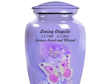 May include: Purple cremation urn with a silver butterfly design and the text "Loving Angeila 2-3-1950 - 2-2-2022 Forever Loved and Missed".