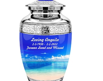 May include: Silver cremation urn with a blue and white beach scene and the inscription "Loving Angeila 2-3-1950 - 2-2-2022 Forever Loved and Missed".