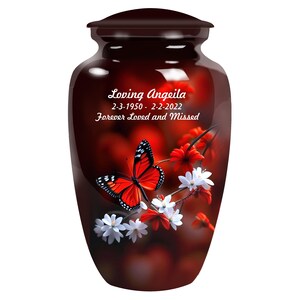 Op de afbeelding: Een donkerbruine keramische urn met een rood en wit vlinderontwerp. De urn heeft de tekst "Loving Angeila 2-3-1950 - 2-2-2022 Forever Loved and Missed" aan de voorkant.