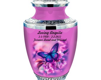 May include: Pink cremation urn with a silver lid and trim. The urn features a butterfly with purple and blue wings on a floral background. The text on the urn reads "Loving Angeila 2-3-1950 - 2-2-2022 Forever Loved and Missed".