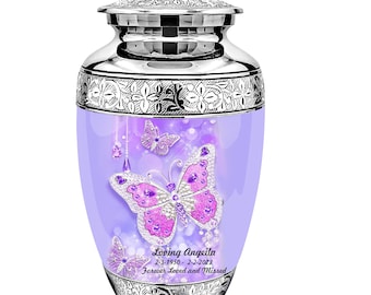 May include: A silver and purple cremation urn with a butterfly design. The urn has a floral pattern around the top and bottom. The text "Loving Angella 2-3-1950 - 2-2-2022 Forever Loved and Missed" is printed on the urn.