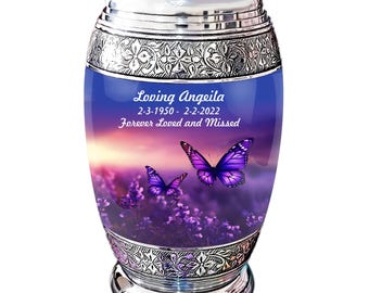 May include: Silver urn with a purple and blue sunset scene with two purple butterflies. The urn has the text "Loving Angeleila 2-3-1950 - 2-2-2022 Forever Loved and Missed" on the front.