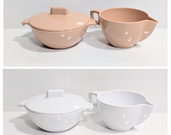 May include: Two sets of serving dishes. The top set is a light peach color, including a lidded bowl and a pitcher with a handle and spout. The bottom set is white, with a similar lidded bowl and pitcher design.