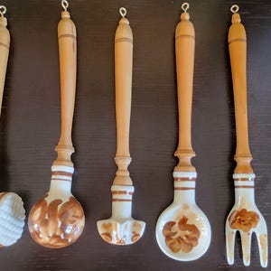 Puede incluir: Conjunto de seis utensilios de cocina de cerámica con mangos de madera. Los utensilios están pintados con diseños florales marrones y blancos. El conjunto incluye un machacador de patatas, un batidor, una cuchara, una cuchara, un tenedor y una espátula.