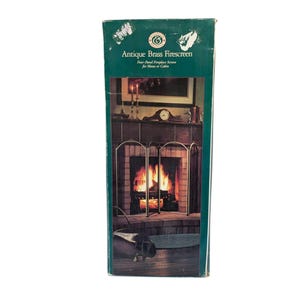 May include: A green box with the words "Antique Brass Firescreen" printed on it. The box shows a four-panel fireplace screen in front of a fireplace with a fire burning. The box is for home or cabin use.