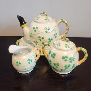 Puede incluir: Un juego de té blanco con diseños de trébol verde. El juego incluye una tetera, una jarra de crema, un azucarero y un plato.