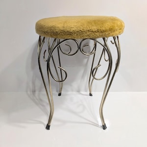 May include: A vintage vanity stool with a round, mustard-yellow plush seat. The metal frame is a light gold colour with decorative scrollwork and curved legs. The stool has a classic, elegant design.