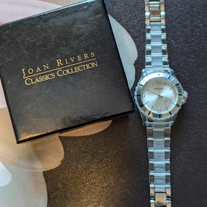 May include: A silver Joan Rivers Classics Collection watch with a white face and silver band. The watch is in its original box.
