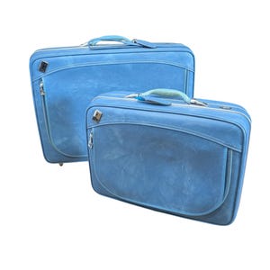 Peut inclure: Deux valises bleues vintage assorties. La plus grande valise a une forme rectangulaire avec une poche avant incurvée et une fermeture éclair. La plus petite valise est de conception similaire. Les deux ont des poignées bleu clair et des ferrures argentées.
