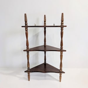 Peut inclure: Étagère d'angle en bois brun foncé à trois niveaux. Les étagères triangulaires sont soutenues par des colonnes torsadées et surmontées de finials décoratifs. Conçue pour s'intégrer dans un coin, elle optimise l'espace.