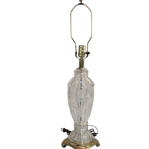 May include: A clear glass table lamp with a gold base and a cut glass design. The lamp has a simple, elegant design.