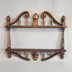May include: A two-tiered shelf unit with a decorative, ornate design. The shelf is made of wood and painted in a copper color. The shelf has a scalloped top and bottom edge with decorative finials.
