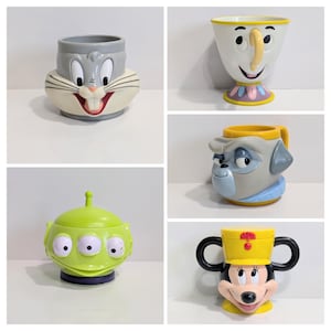 May include: A selection of character mugs featuring Bugs Bunny, Chip, a Paw Patrol character, a Little Green Men alien, and Minnie Mouse. Each mug has a unique design with bright colours and character details, perfect for collectors.