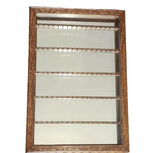 May include: A wooden display case with glass panels and carved details. The case has five shelves with small slots for holding items.