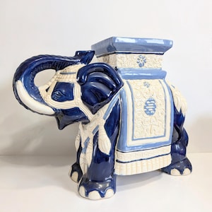 Puede incluir: Un taburete de jardín con forma de elefante de cerámica en una llamativa combinación de colores azul y blanco. El elefante presenta detalles intrincados, incluyendo una silla decorativa y una parte superior cuadrada. El diseño incorpora patrones florales y geométricos.