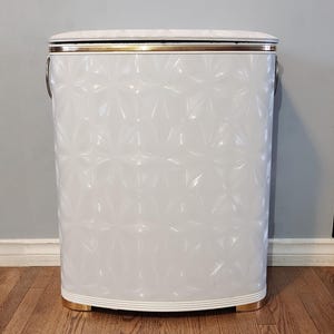 May include: White laundry hamper with a gold trim and a diamond pattern. The hamper has two metal handles on the sides.