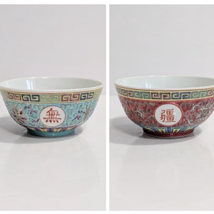 May include: Two decorative ceramic bowls. One bowl is turquoise with a floral design and a Chinese character. The other bowl is red with a floral design and a Chinese character. Both bowls have a white interior.