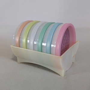 May include: Set of six pastel-colored plastic coasters with a white plastic holder. The coasters are stacked in a rainbow pattern, with the pink coaster on top and the orange coaster on the bottom.