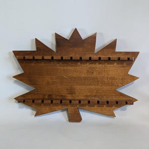 May include: A wooden maple leaf-shaped jewelry organizer with a dark brown finish. The organizer has multiple slots for hanging necklaces or earrings. The leaf design features pointed edges and a stem at the bottom, creating a decorative and functional piece.