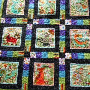 May include: A colorful quilt with a black background and a variety of animal and nature scenes in squares. The quilt features a fox, a skunk, an owl, a bird, and other animals.