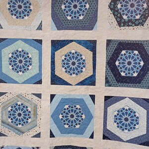 May include: A quilt with a geometric pattern in shades of blue, white, and beige. The quilt is made up of squares with a central octagon shape. The octagons are surrounded by a border of smaller squares.