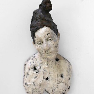 May include: A white ceramic bust sculpture of a person with a small monkey sculpture on top of their head.