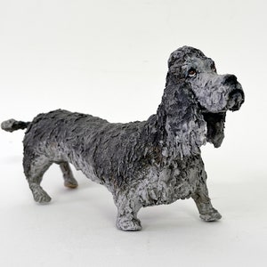 May include: A handcrafted sculpture of a dog, primarily in shades of gray and black. The dog has long, floppy ears and a textured surface, giving it a unique, artistic appearance. The sculpture is standing on all fours.