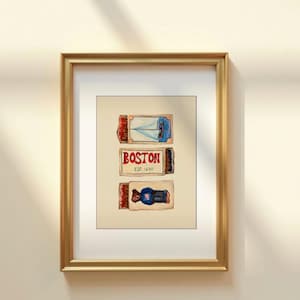 May include: Framed artwork showing three illustrated matchboxes. The top matchbox depicts a sailboat, the middle one reads "BOSTON EST. 1630", and the bottom one shows a person. The artwork is in a gold frame.