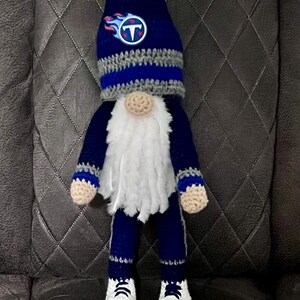 May include: A handmade gnome doll in navy blue and gray, with a white beard and white sneakers. The gnome's hat features the Tennessee Titans logo. The doll is crocheted and has a whimsical design.