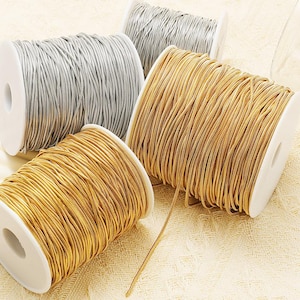 Puede incluir: Carretes de cordón metálico dorado y plateado. Los carretes son blancos con el cordón enrollado alrededor. El cordón dorado es de un color cálido y brillante, mientras que el cordón plateado tiene un aspecto frío y reflectante. El cordón parece fino y flexible.