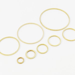 Könnte beinhalten: Ein Satz von acht goldfarbenen Metallringen in verschiedenen Größen. Die Ringe sind in einem Halbkreis auf weißem Hintergrund angeordnet.