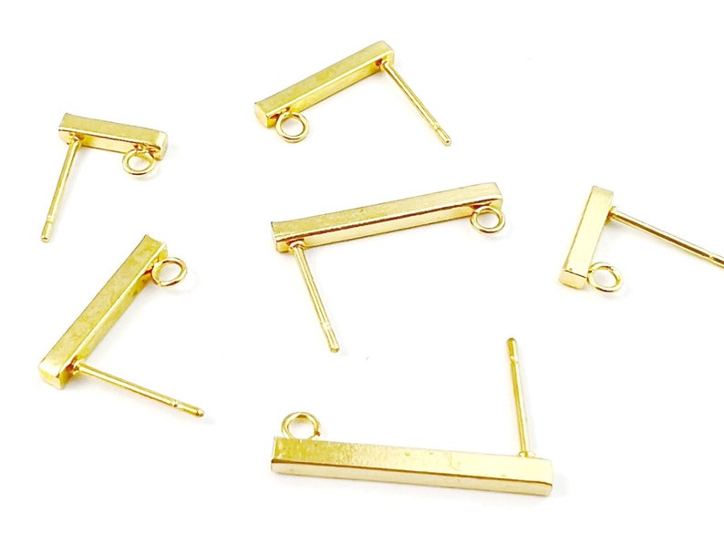 Pu&ograve; includere: Cinque perni per orecchini dorati con una barra rettangolare e un piccolo anello in cima. I perni sono progettati per realizzare orecchini.