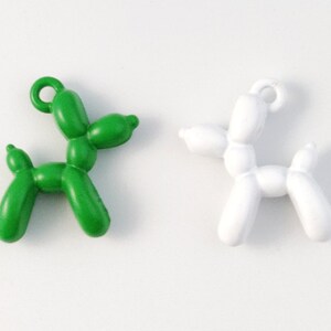 May include: Two balloon animal charms, one green and one white, shaped like a dog. The charms have a loop at the top for attaching to a necklace or bracelet.