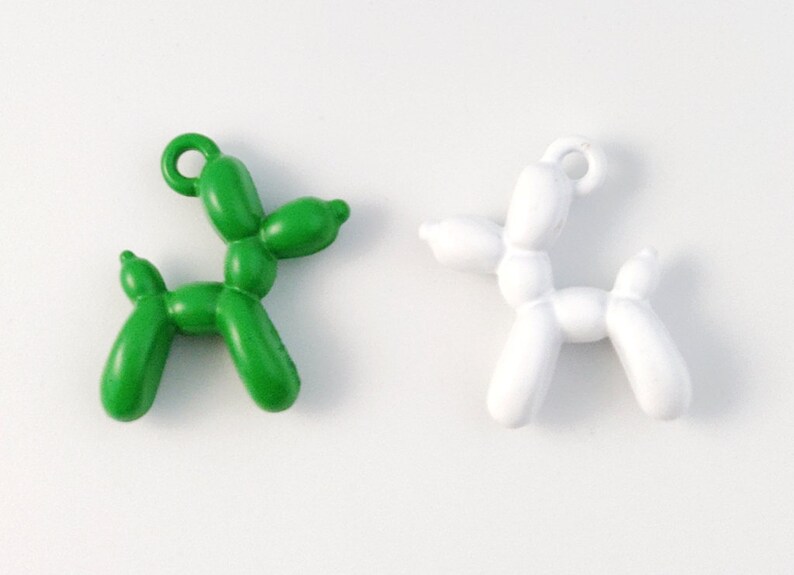 May include: Two balloon animal charms, one green and one white, shaped like a dog. The charms have a loop at the top for attaching to a necklace or bracelet.