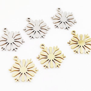 Op de afbeelding: Zes sneeuwvlokcharms, drie zilver en drie goud, met een lus aan de bovenkant om aan sieraden of andere knutselwerken te bevestigen.
