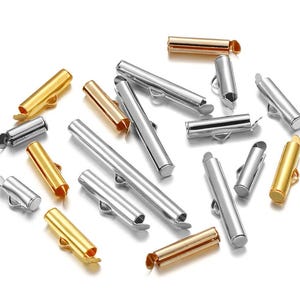 Könnte beinhalten: Sortiment an Metall-Endkappen für die Schmuckherstellung. Die Endkappen sind in Gold-, Silber- und Roségoldtönen gehalten. Sie sind alle zylindrisch geformt und haben an einem Ende eine kleine Schlaufe.