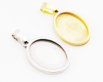 May include: Two oval pendant trays, one gold-toned and one silver-toned, are displayed against a white background. The pendants have a loop at the top for a chain. The gold pendant has a double-layered frame.