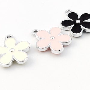 May include: Three silver flower charms with enamel paint. The flowers are white, pink, and black.