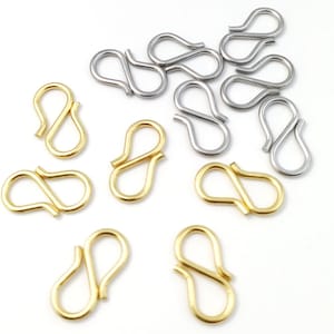 Op de afbeelding: Een verzameling gouden en zilveren S-vormige sluitingen. De sluitingen zijn gemaakt van metaal en worden gebruikt om sieraden of andere voorwerpen aan te bevestigen.