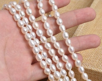 May include: Several strands of white oval pearls. The pearls are strung together, forming a necklace or bracelet. The pearls have a smooth, lustrous surface and a creamy white colour. The background is a neutral tan colour.